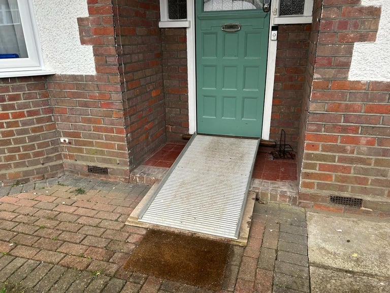Completed — aluminium disability access ramp installed leading to the green front door with red brick surroundings