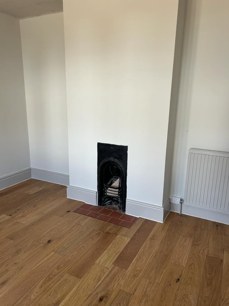 Recently refurbished empty room with wooden floor, freshly painted white walls, and a black fireplace insert