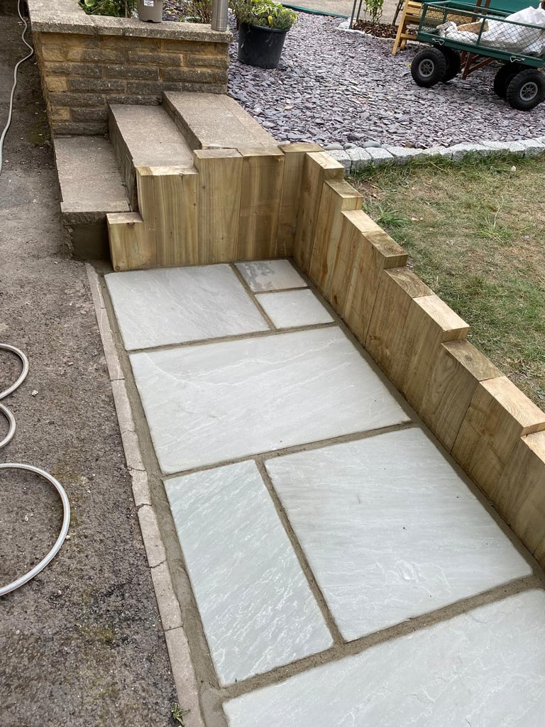 Newly constructed outdoor seating area with wooden fence and light-colored paving stones bordered by concrete edging