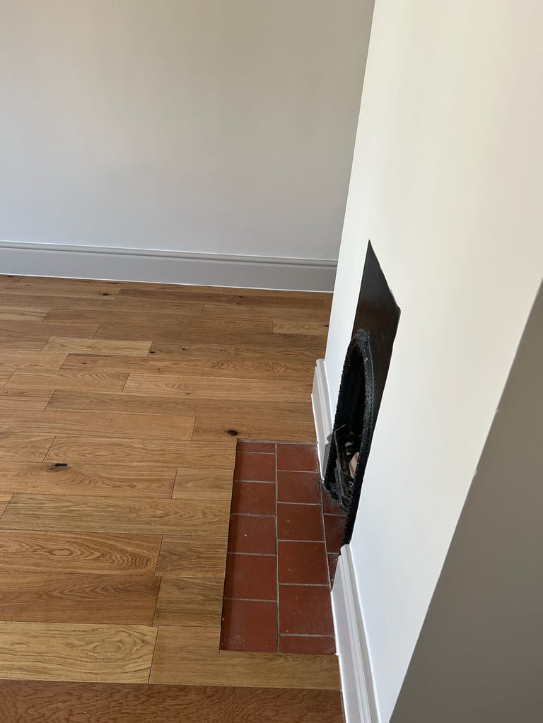 Interior corner showing transition between wood and tile flooring with white baseboard and wall