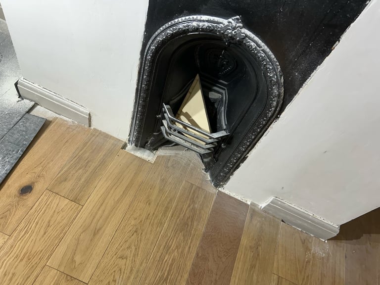 View looking up at an open ceiling vent with dark metal ductwork containing papers and materials inside, above a wooden floor