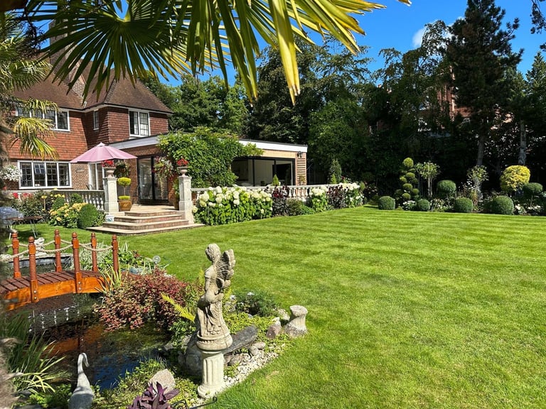 Brick residential house with large manicured lawn, palm trees, garden statue, and ornamental plants in sunny backyard setting
