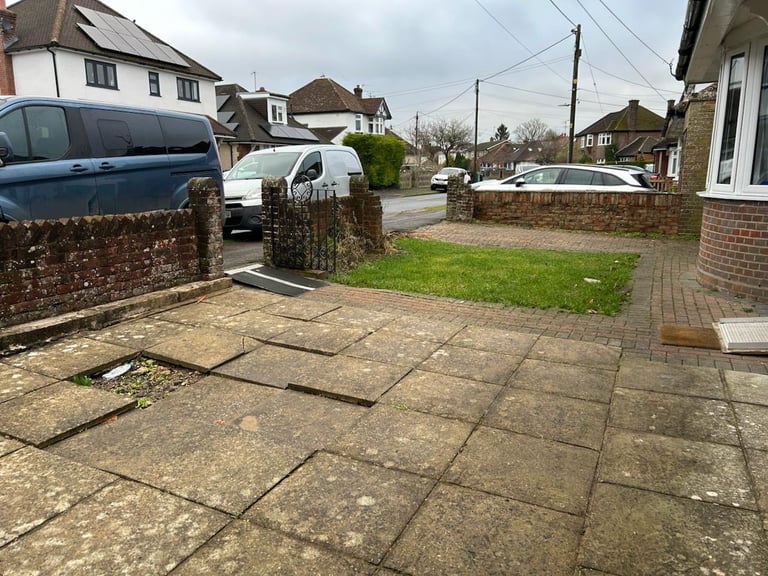 Before — original residential driveway with paved tiles, parked cars, and brick wall along a quiet suburban street
