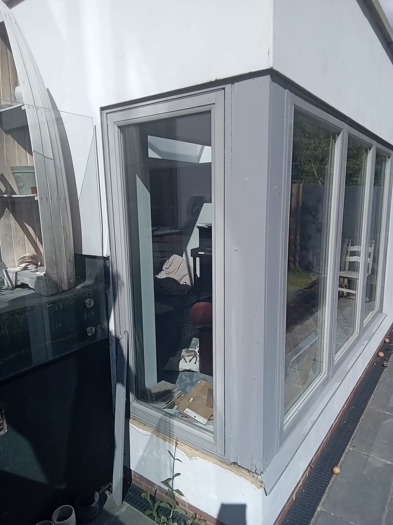 Small white storage shed or utility room with glass doors and windows, containing various household items and boxes