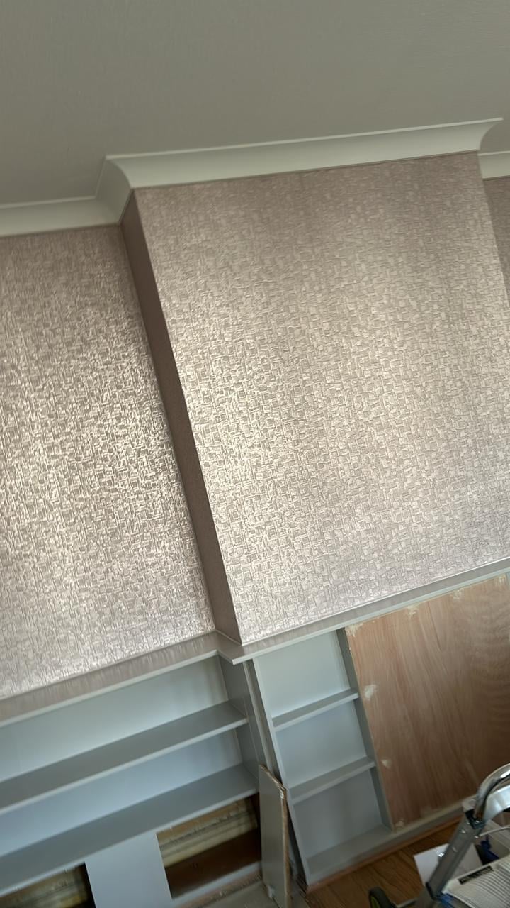 Close-up of textured metallic wallpaper installation with white trim and baseboard