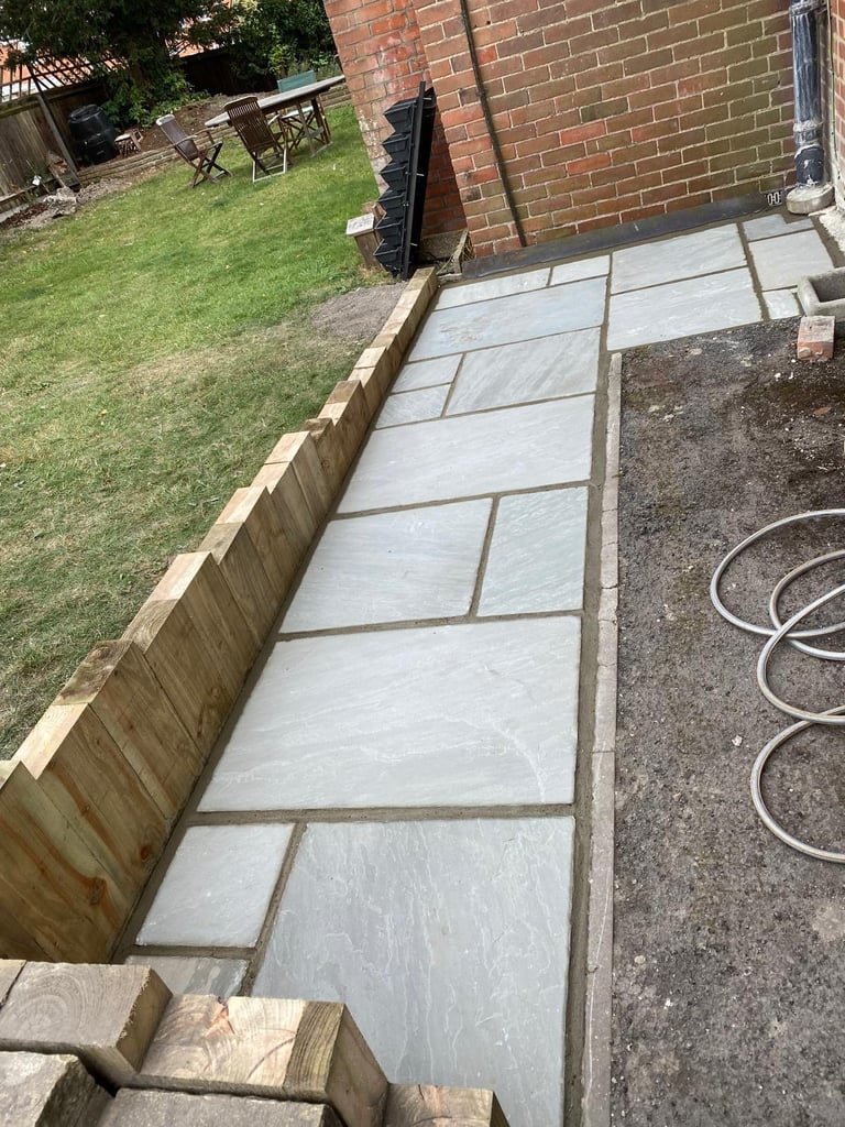 Newly laid patio with large slate tiles in a backyard next to a brick house and wooden fence