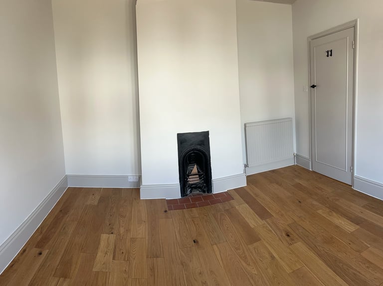 Empty room with white walls, wooden floor, fireplace insert in center wall, and door on right side