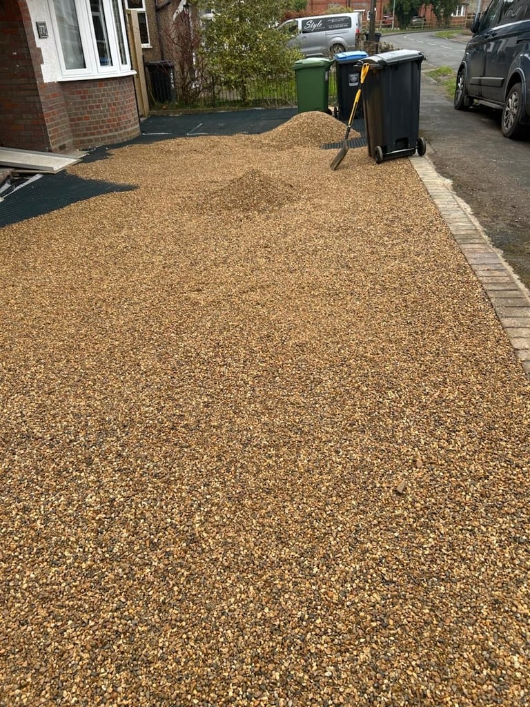 Completed — fully covered residential driveway with tan and brown gravel, bordered by the brick house
