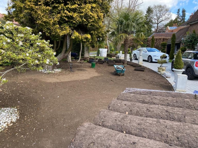 Residential driveway with gravel area, white car parked in background, trees and landscaping visible