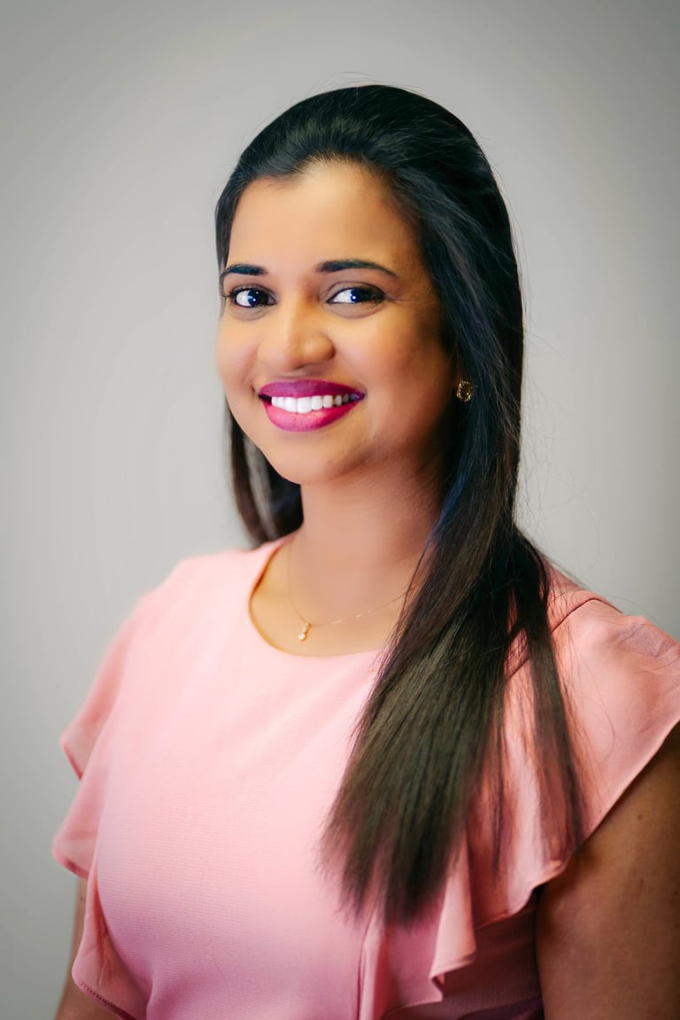 Portrait of a young woman with long dark hair wearing a pink top, smiling against a gray background