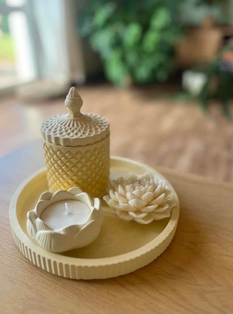 Cream-colored decorative candle set with textured jar, lotus flower, and teacup holder on wooden table