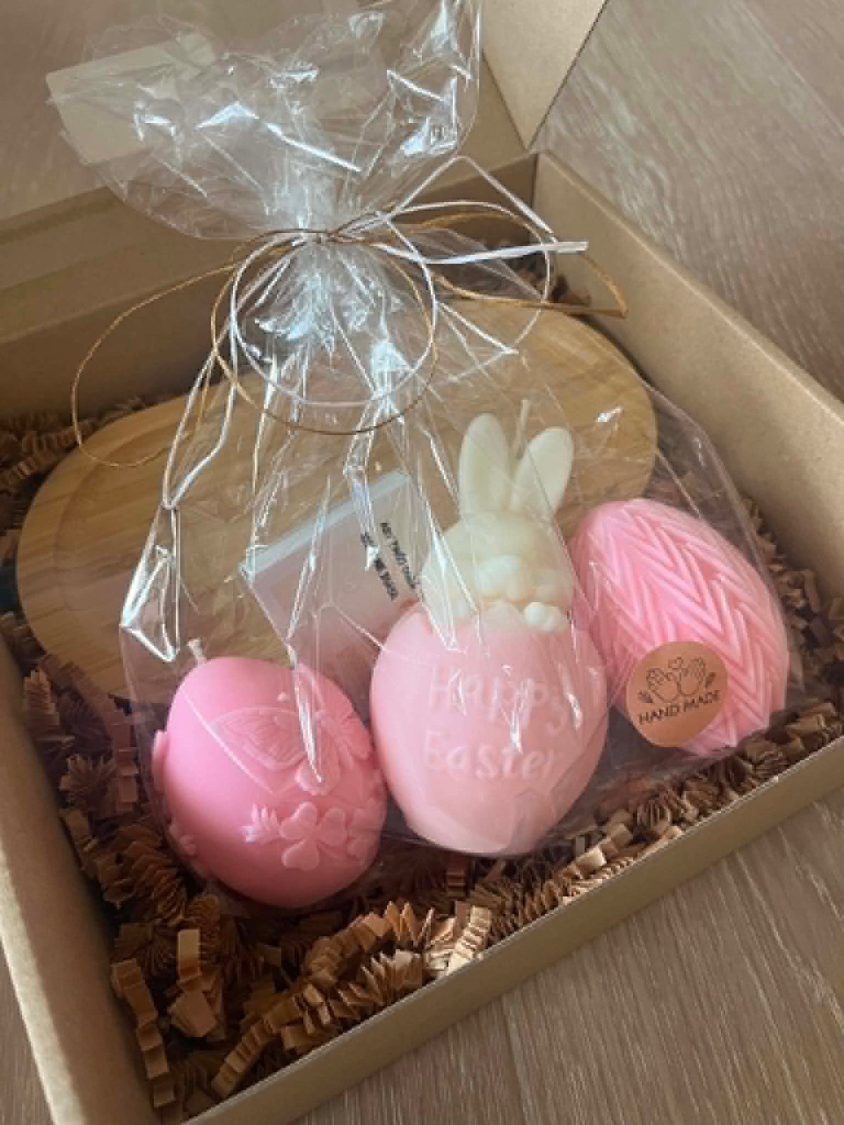 Gift box containing pink bath bombs, a white ceramic bunny, and decorative straw packaging with cellophane wrap