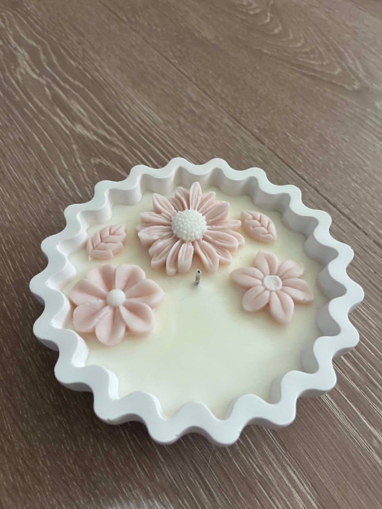 White decorative cake with pink fondant flowers and wavy scalloped edges on wooden surface
