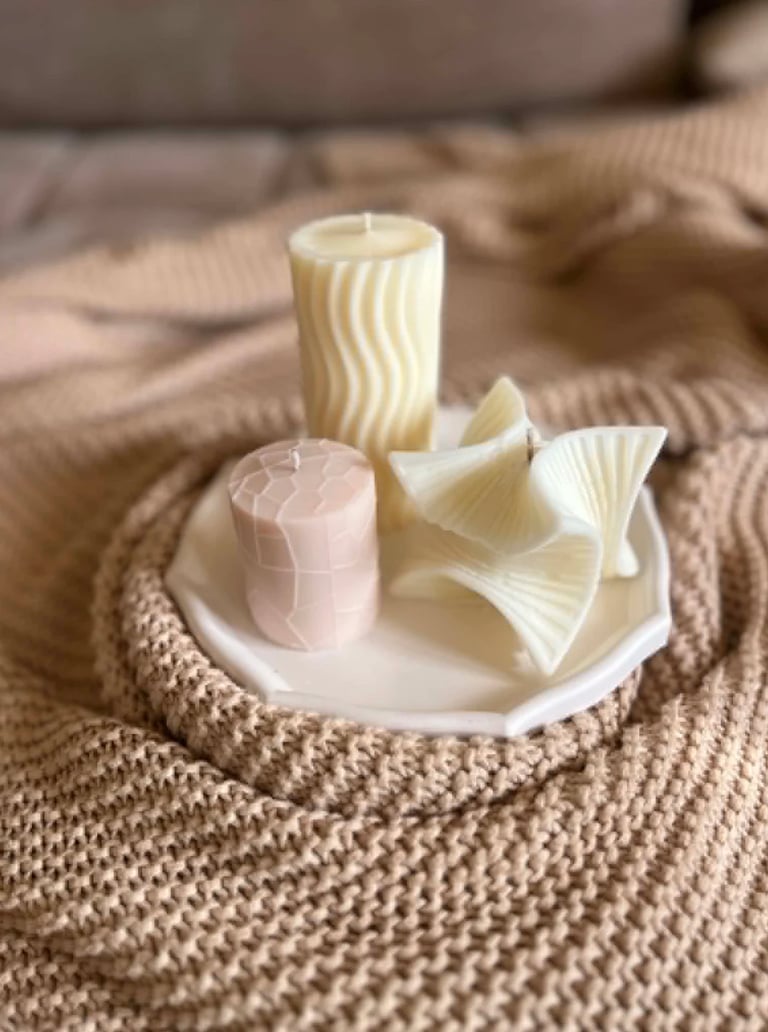 Three decorative candles on a white ceramic holder placed on a beige knitted blanket