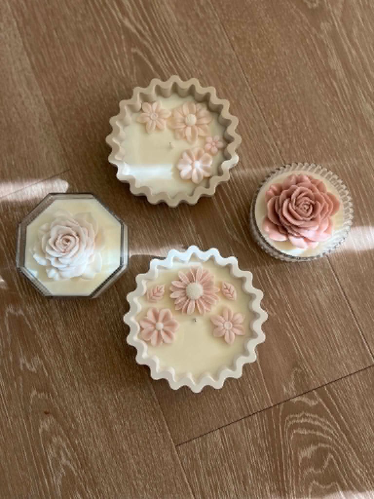 Four decorative wax candles with floral designs in pink and cream on a wooden surface