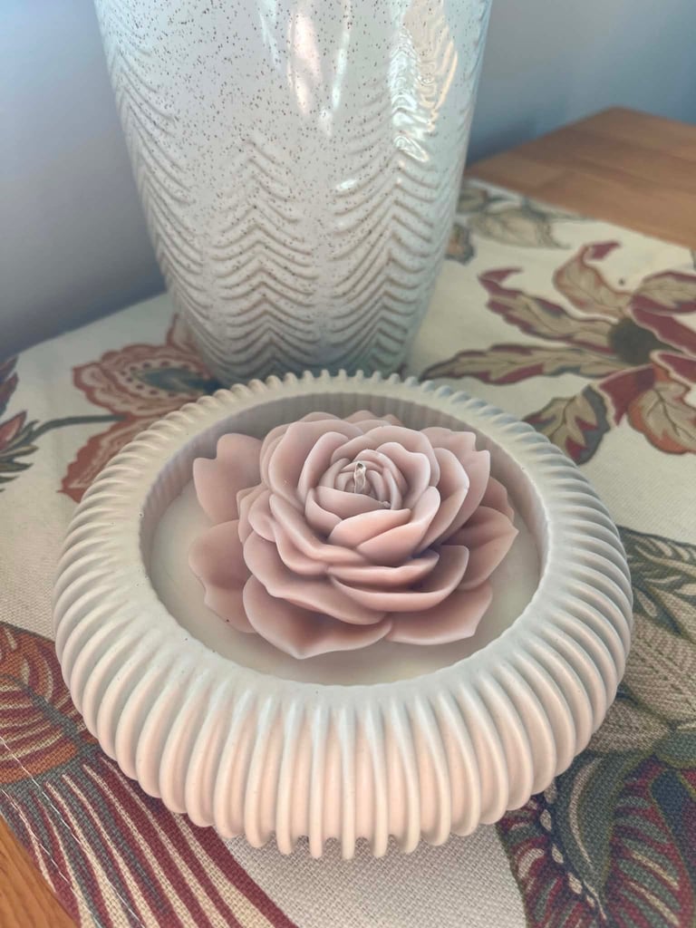 Pink decorative rose candle in white ribbed ceramic holder on floral patterned fabric