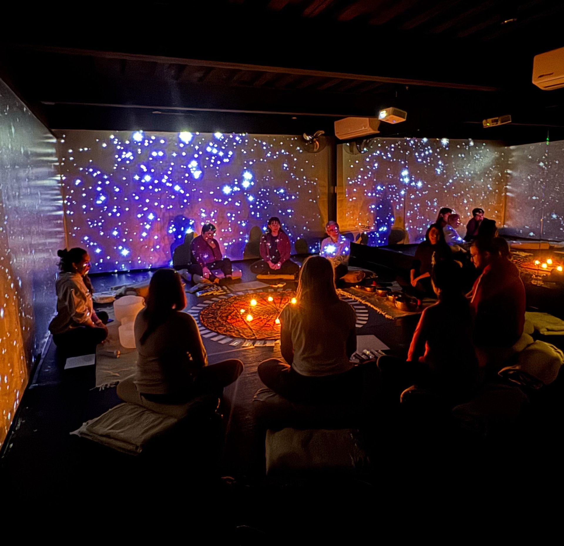 Group of people sitting in a dark immersive space with blue and orange star-like lights on walls and warm floor lighting