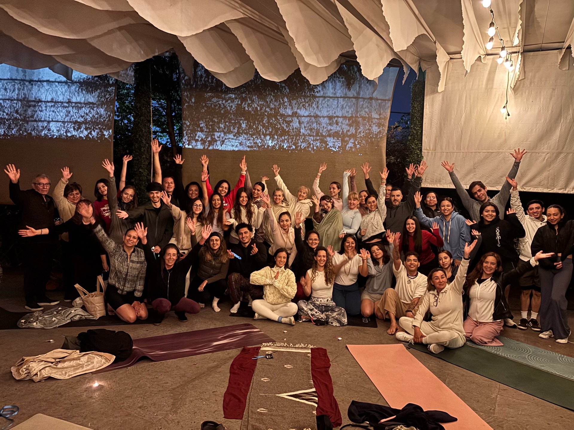 Group of diverse people posing together indoors under fabric canopy with raised arms and hands in celebratory gesture