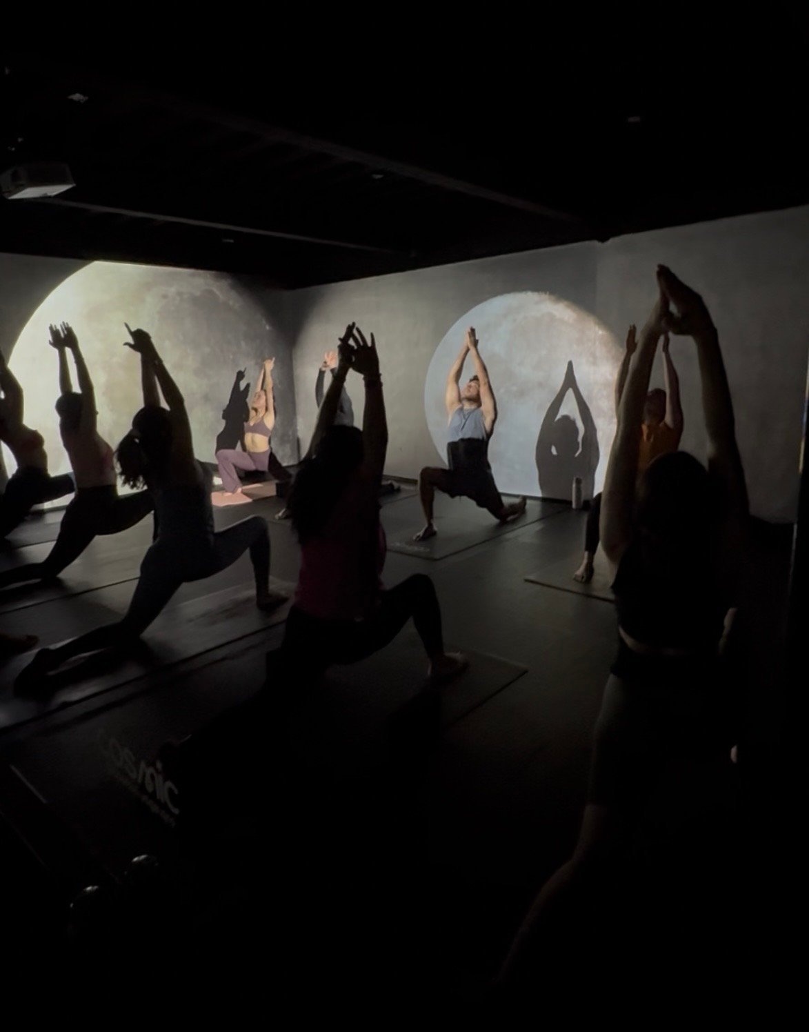 Group of people practicing yoga poses in a studio with illuminated circular moon-like backlit panels on the walls