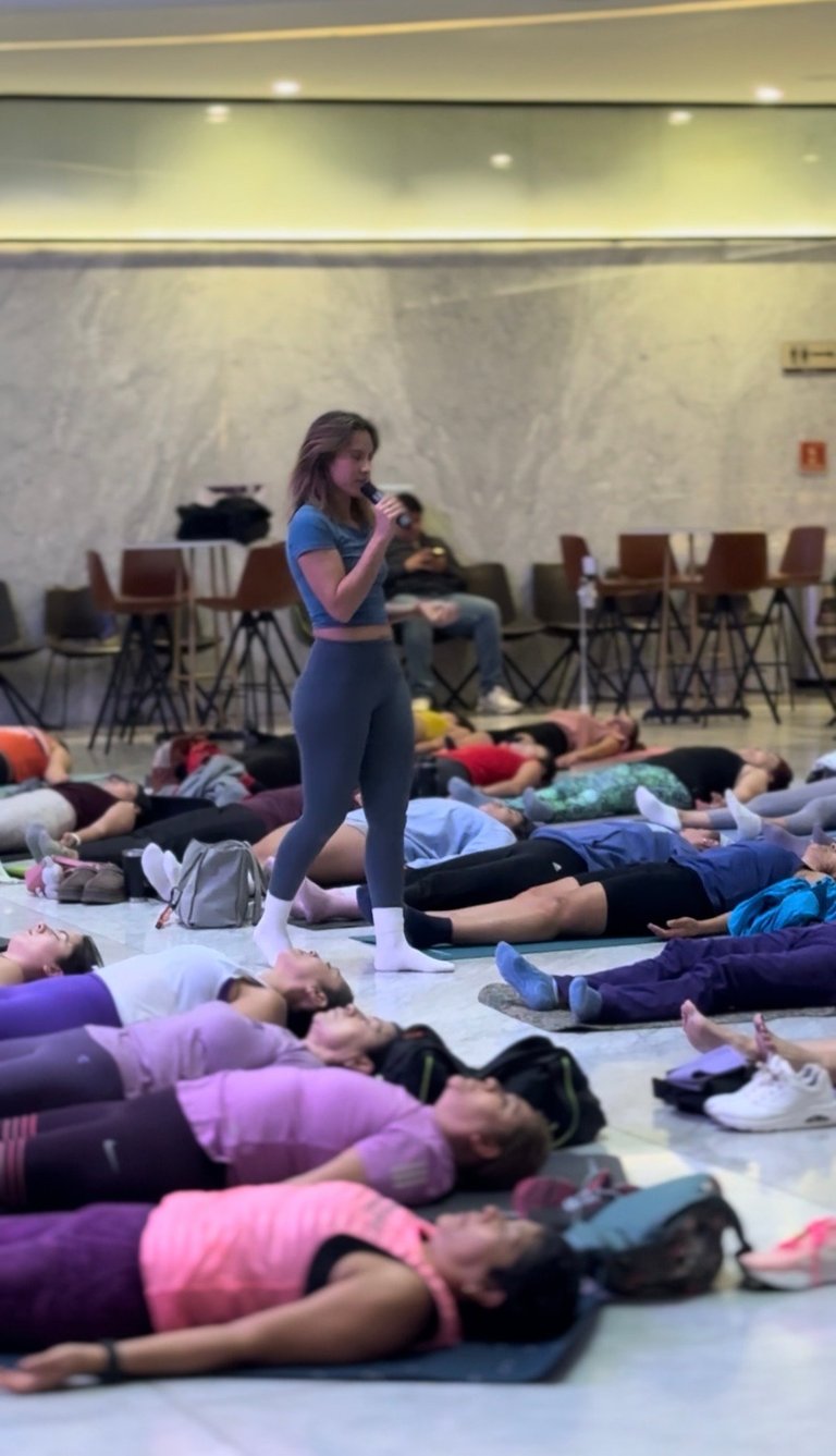 Fitness instructor leading a group exercise class in an indoor studio with participants lying on the floor