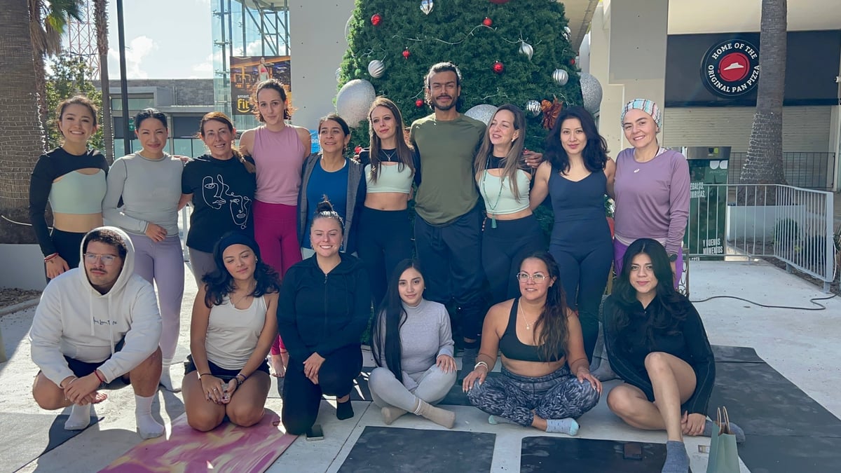 Group fitness class posing together indoors with yoga mats, Christmas tree visible in background
