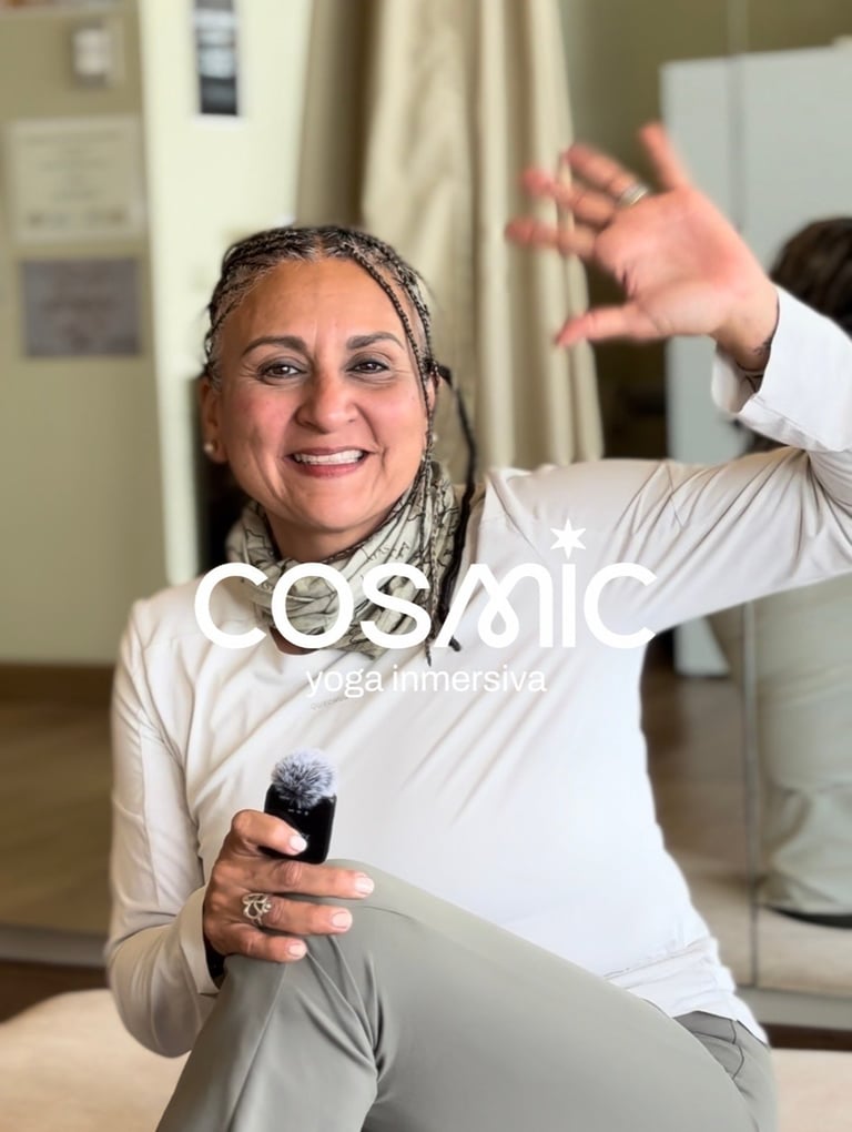 Woman with braided hair smiling at camera, holding microphone, raising one arm in enthusiastic gesture indoors.