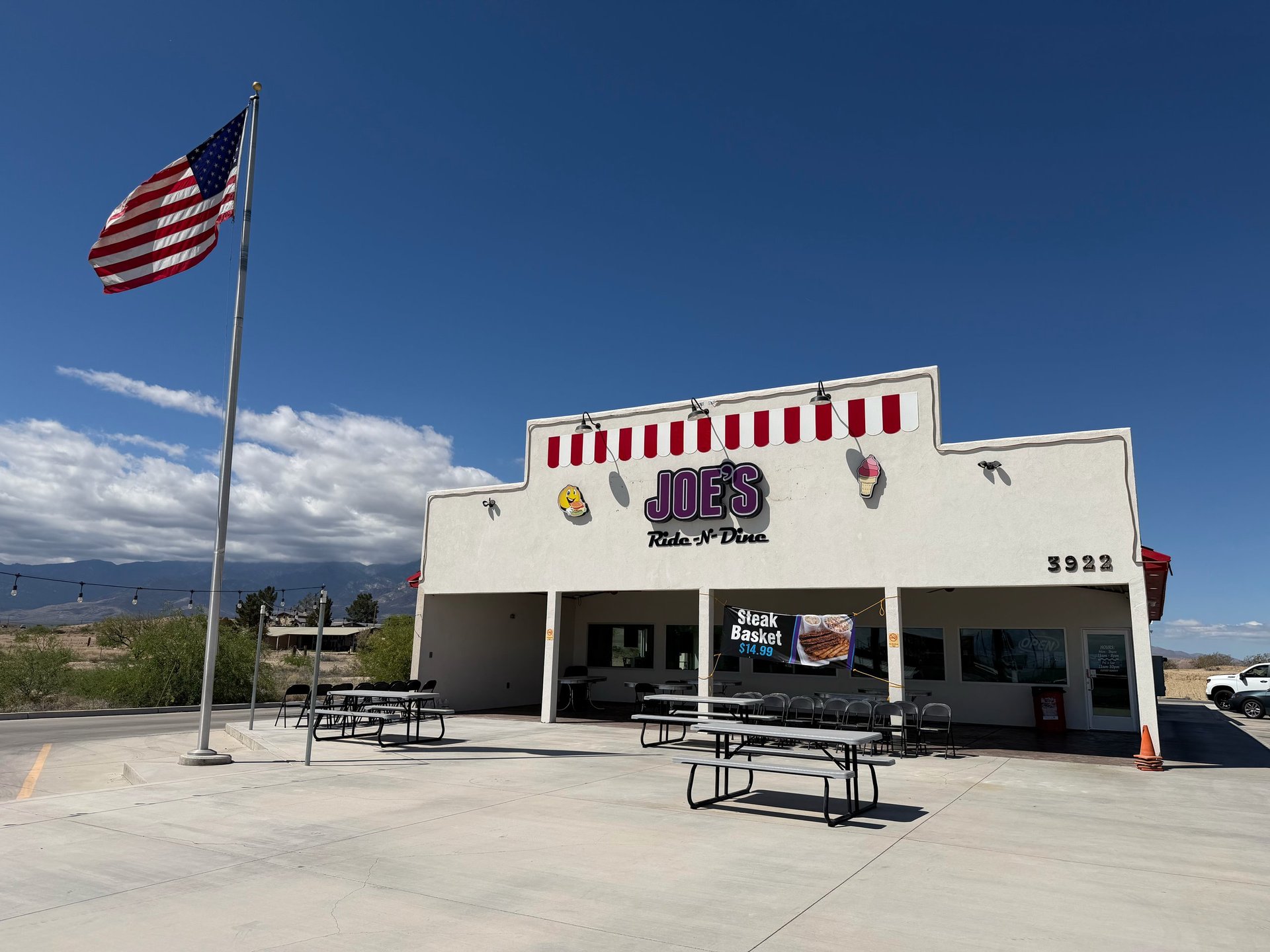 American flag flying in front of a retro diner with red and white striped awning and outdoor seating on a sunny day