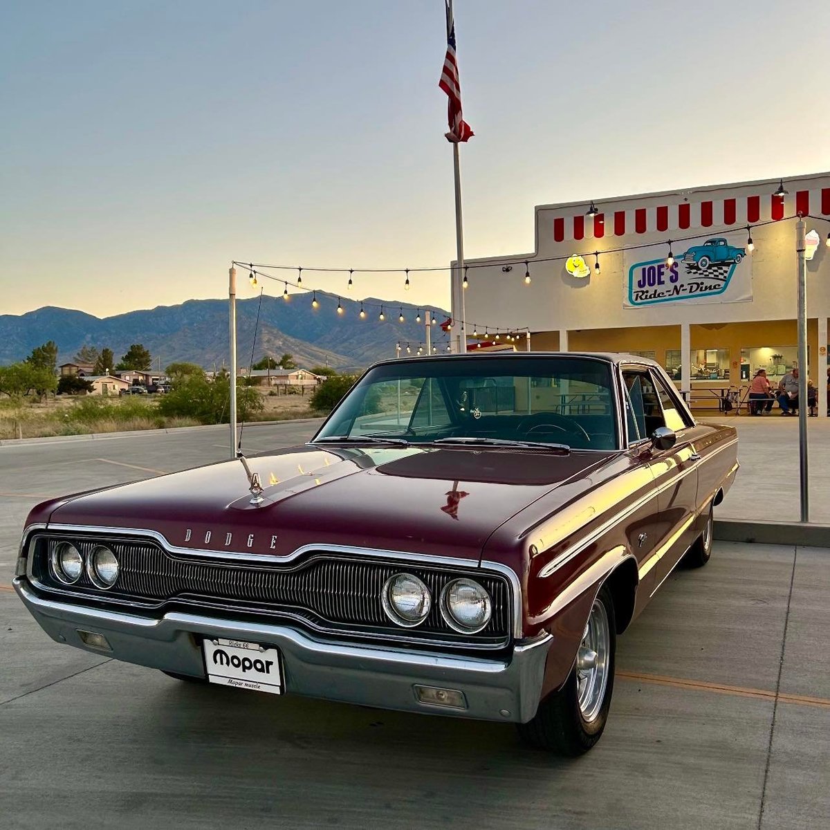 Vintage maroon and gold Dodge Mopar parked outside a diner with mountains in the background