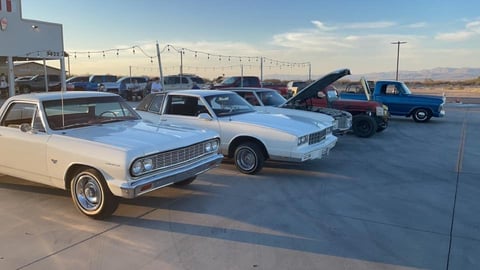 Row of classic American cars from 1960s parked at outdoor car show with desert mountains in background