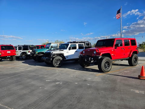 Row of modified Jeeps and vehicles parked in lot with American flag, clear blue sky above