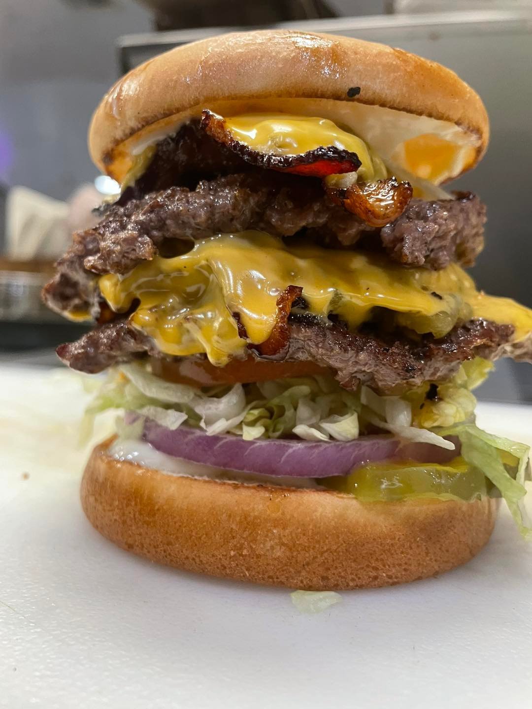 Stacked double cheeseburger with melted yellow cheese, crispy bacon, lettuce, and red onion on a toasted bun