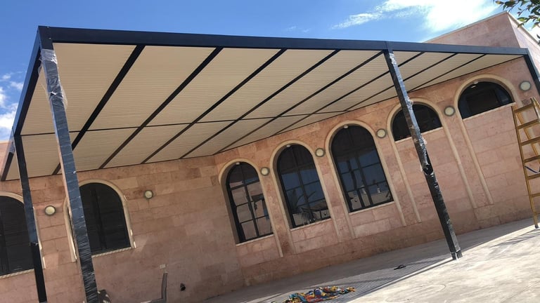 פרגולת אלומיניום מודרנית עם גג בד בז' מכסה חצר של בניין אבן עם חלונות קשתיים