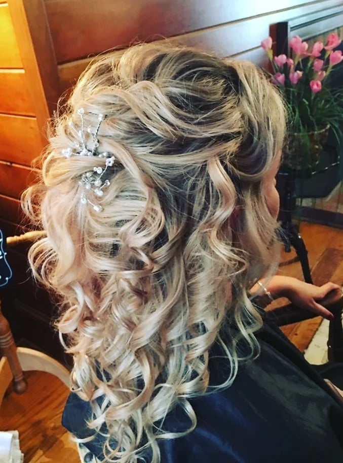 Long, wavy blonde hair finished with a decorative crystal accessory for a formal event.