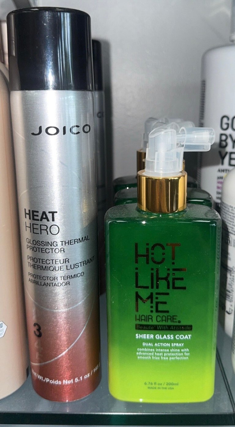 Joico Heat Hero Glossing Thermal Protector and Hot Like Me Sheer Glass Coat Dual Action Spray on a salon shelf.
