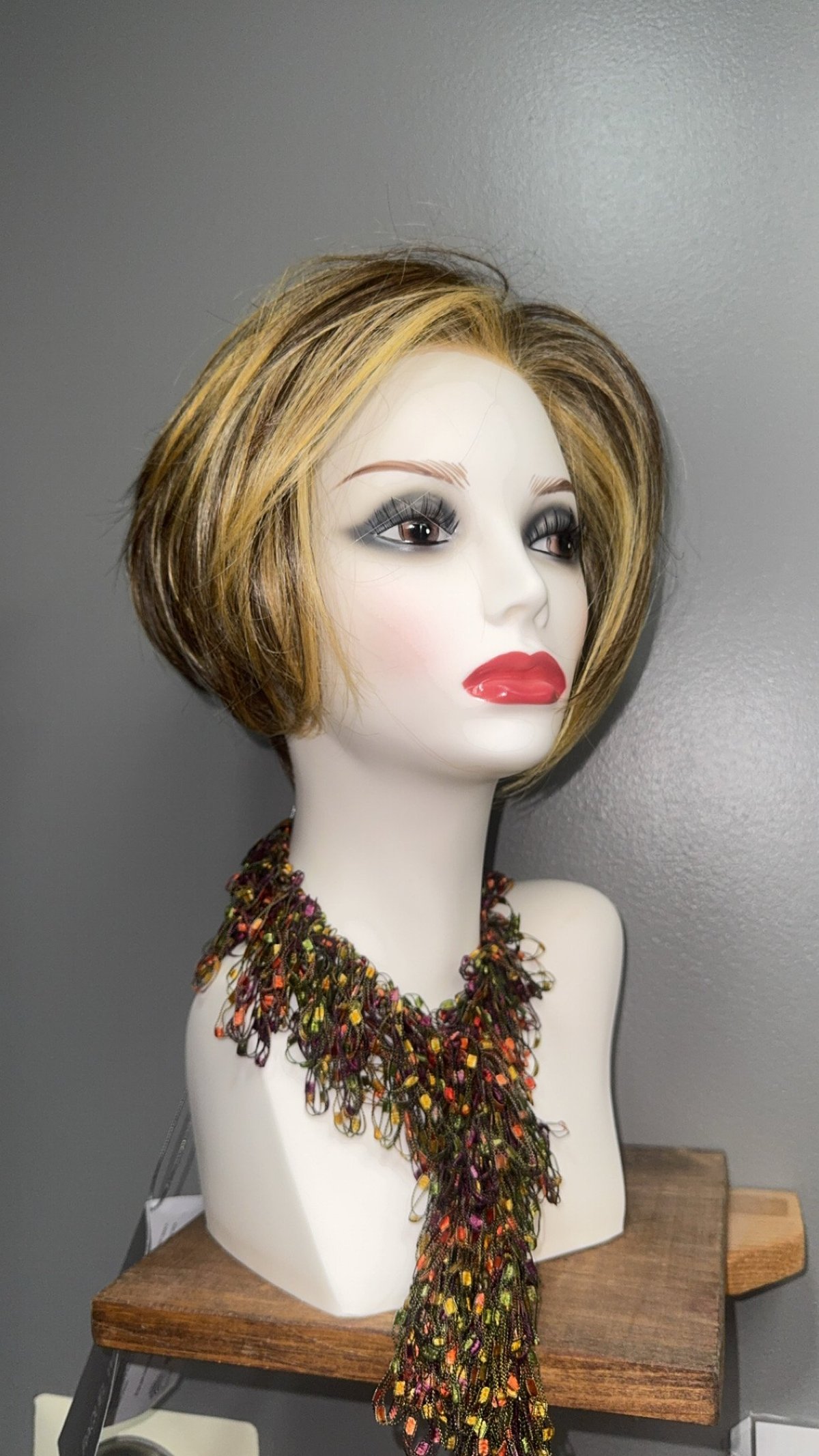 Mannequin head with short layered blonde-brown hair on a wooden stand.