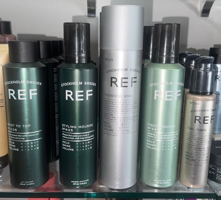REF Stockholm Root to Top, Styling Mousse, Thickening Spray, Fiber Mousse, and Curl Power products displayed on a salon shelf.