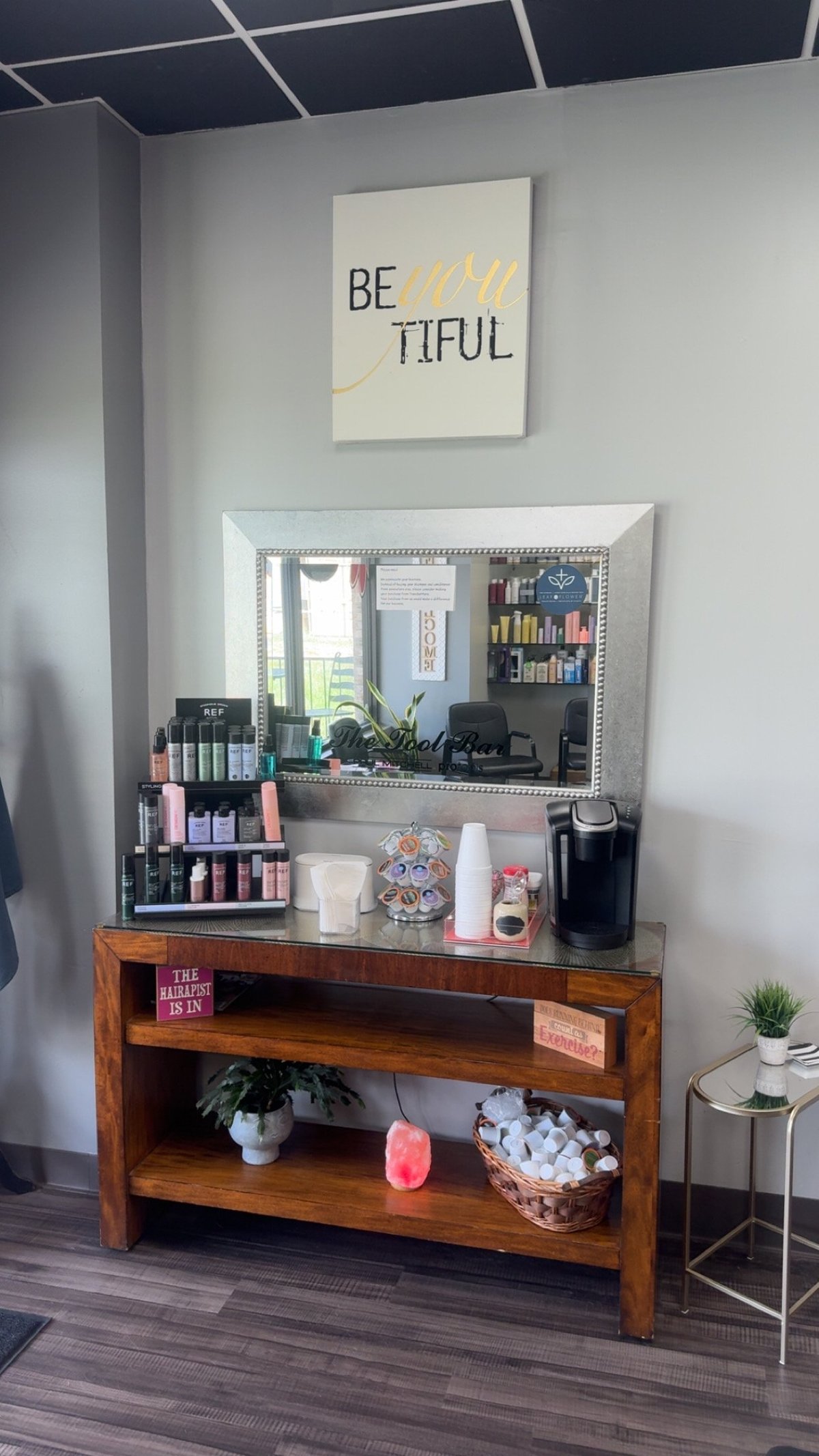 Be-YOU-tiful wall art above a wood vanity and tool bar with products, a Keurig, and organized supplies