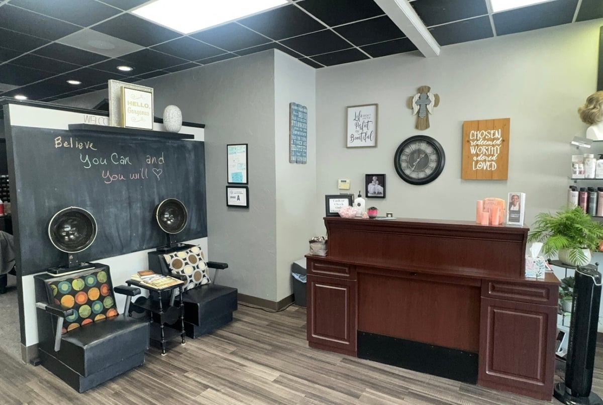 Salon reception area with a dark wood desk, decorative wall art, product displays and casual seating