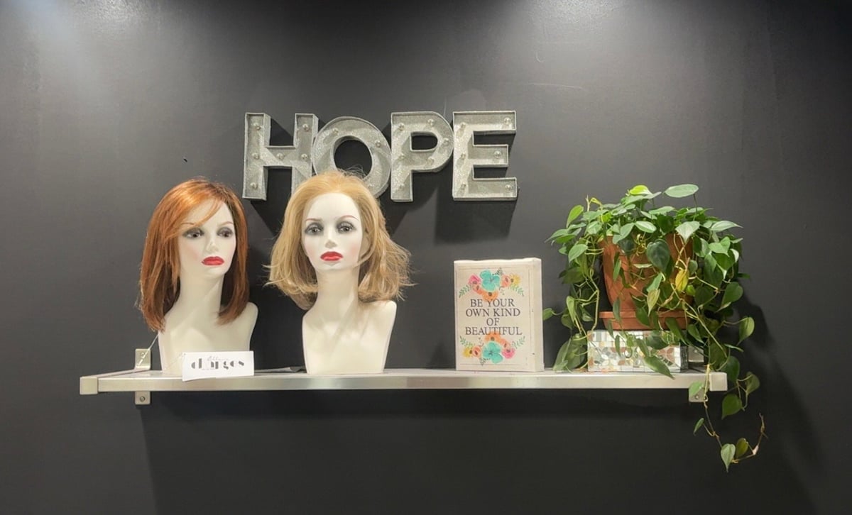 A shelf against a dark wall displaying two mannequin heads with wigs, a decorative sign, a potted plant, and the word HOPE in large letters