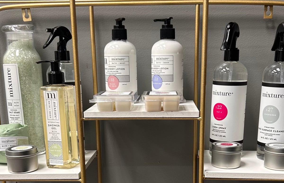 Mixture bath and body products available from Emilie at Trendsetters of Hendersonville, displayed on glass shelves with gold frames.