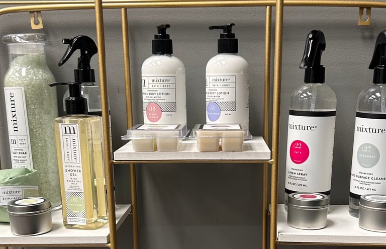 Mixture bath and body products available from Emilie at Trendsetters of Hendersonville, displayed on glass shelves with gold frames.