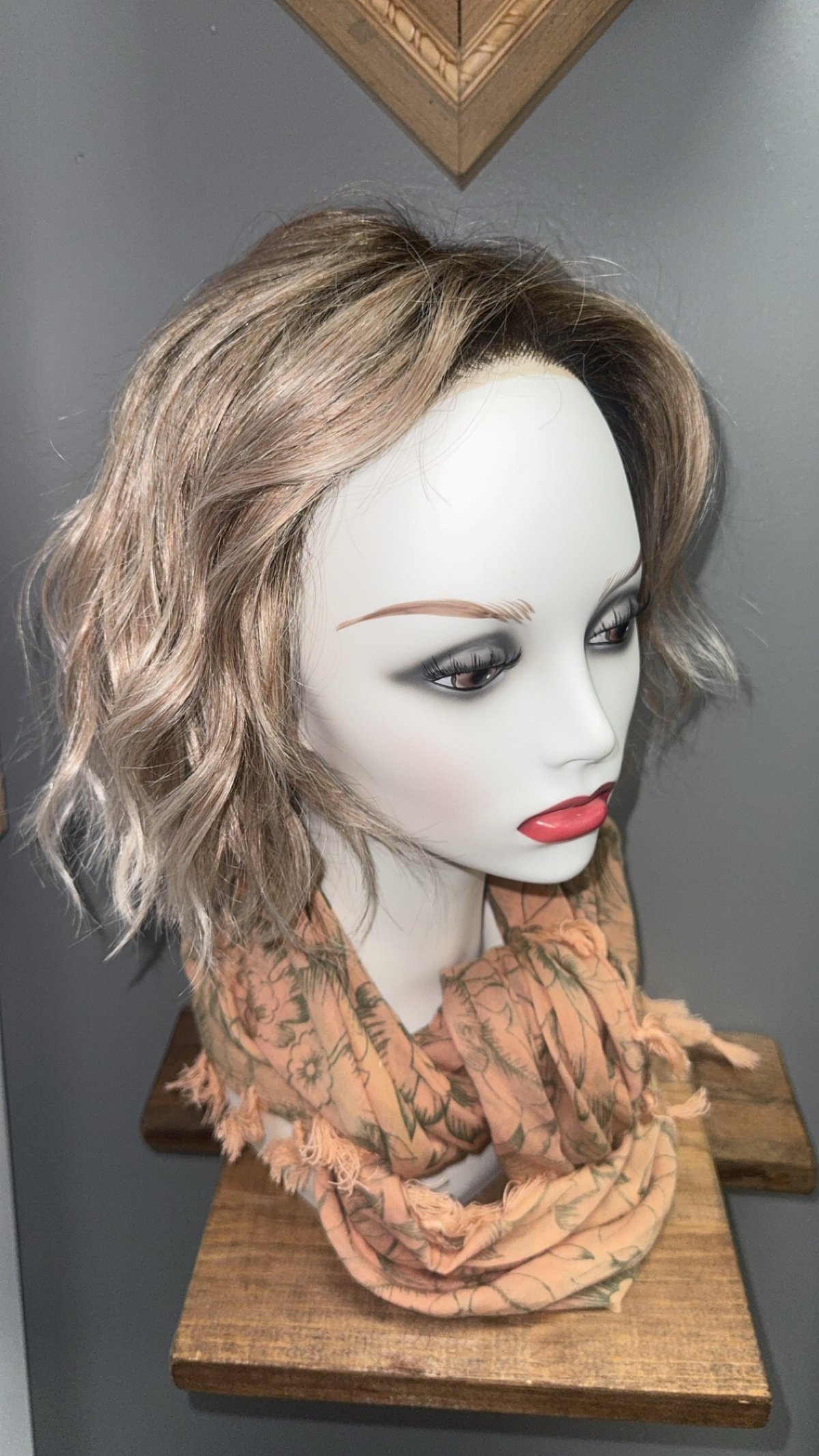 Mannequin head with short wavy brown hair wearing a patterned brown scarf.