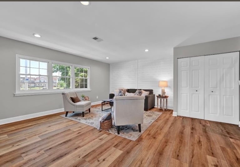 Bright modern living room with hardwood floors, armchairs, sofa, large windows, and white closet doors