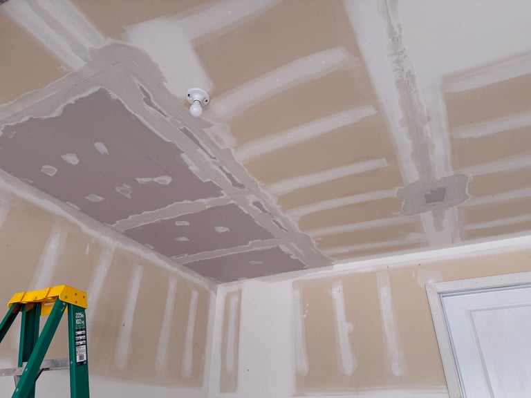 Drywall ceiling installation with exposed studs, joint compound, and green ladder in foreground