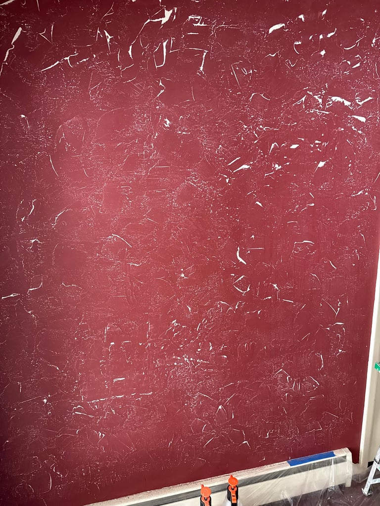 Burgundy textured wall with white chalk scratch marks and protective plastic sheeting at the base