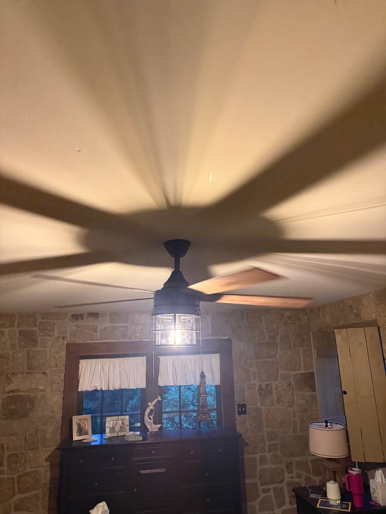 Ceiling fan with light on, creating shadows on textured stone walls in a residential room