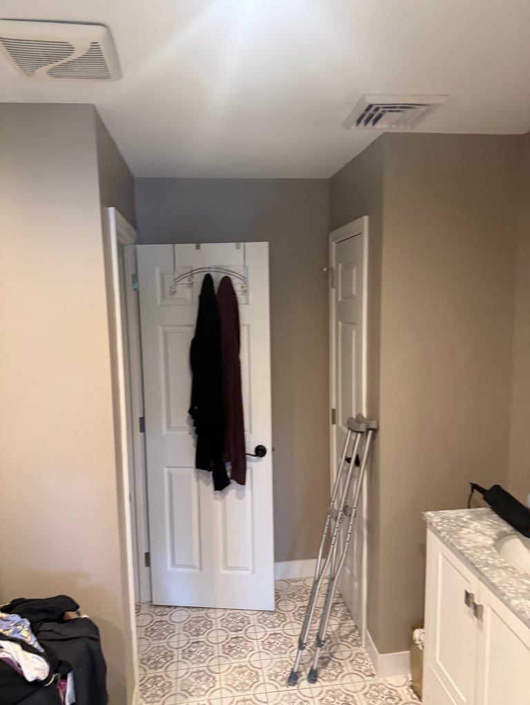 Interior view of a bedroom with beige walls, white trim doors, light fixture on ceiling, and clothes hanging on the back door