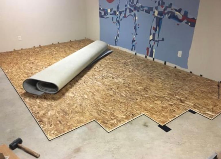 Cork flooring installation with rolled underlayment, partially laid planks, and mallet visible in a room with blue wall mural