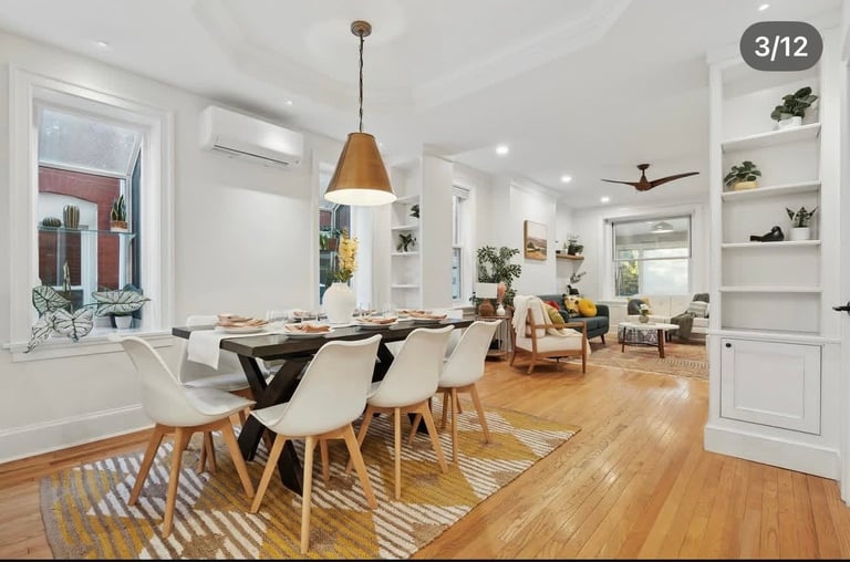 Modern dining room with wooden table, white chairs, pendant light, and open-concept kitchen and living area with hardwood floors