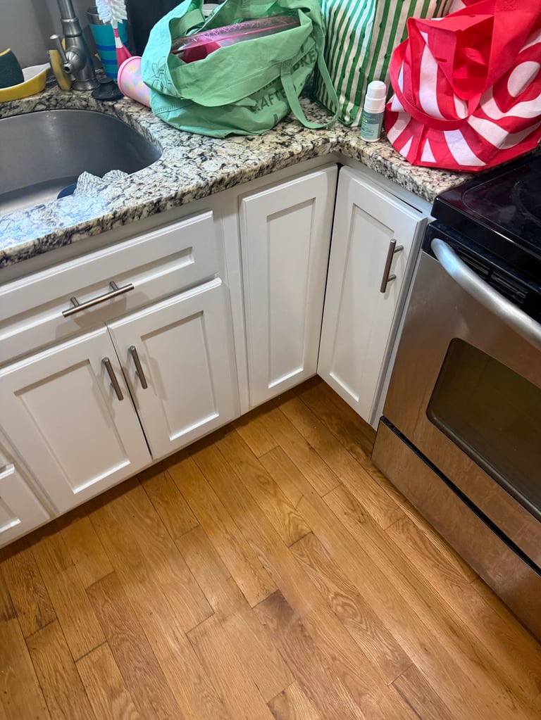 Kitchen corner with white cabinets, granite countertop, reusable shopping bags, and stainless steel oven on wooden floor